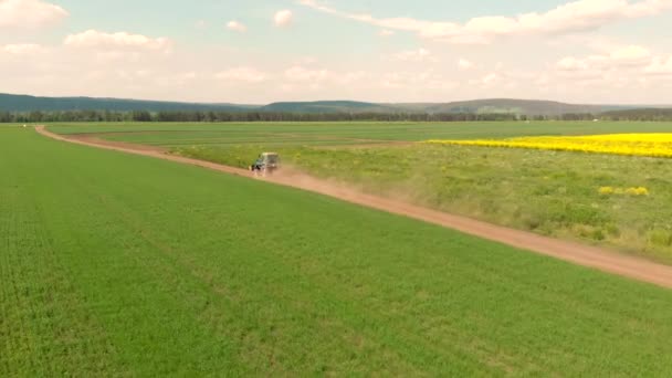 Drone flying over field and blue cultivation tractor driving on a ground road. — Stock Video
