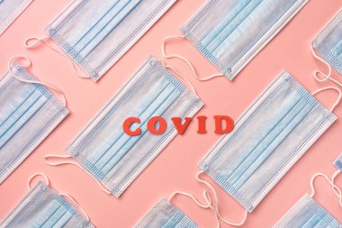 Mavi tıbbi koruma pembe arka planda, solunum hastalıklarına, virüs gribine ve koronavirüse karşı güvenlik için maske takıyor. Covid kelimesi ortada kırmızı harflerle yazılır..