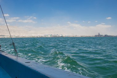 Süveyş Körfezi 'ndeki hareketli bir tekneden gelen görüntüler derin mavi sularda uyanmayı gösteriyor Ras Sedr Mısır' ın uzak kıyı şeridi sisli dağlara karşı bir şehir limanı ve sanayi bölgesini gösteriyor.