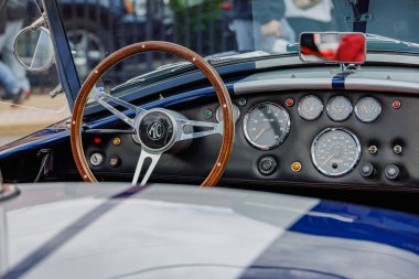 Gösterge paneli, tahta direksiyon, analog enstrümanlar ve krom detayları gösteren klasik bir spor arabanın iç görüntüsü. Klasik araba iç mekanları, klasik yarış, otomotiv tasarımı ve koleksiyoncu araçları ile ilgili konular için ideal.