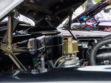 Kaputu açık klasik bir araba motorunun ayrıntılı görüntüsü. Görünür bileşenler arasında hava temizleyici, karbüratör, kablolama ve metal parçalar yer alıyor. Otomotiv temaları, motor tamirleri, araba restorasyonu ve klasik araç koleksiyonları için ideal