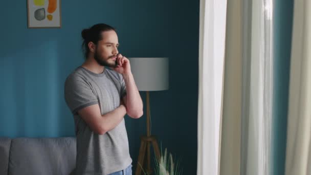 Man praat aan de telefoon, staat bij het raam — Stockvideo