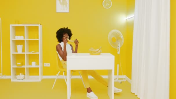 アフリカ人女性が黄色のオフィスでバナナを剥いている — ストック動画