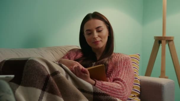 Jovem mulher está lendo livro relaxante no sofá — Vídeo de Stock