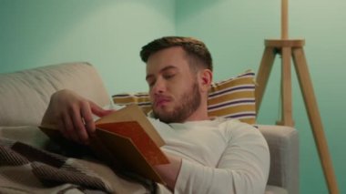 Adam evde kitap okuyor.