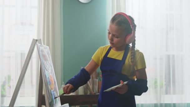Menina pequena em fones de ouvido sem fio é pintura — Vídeo de Stock