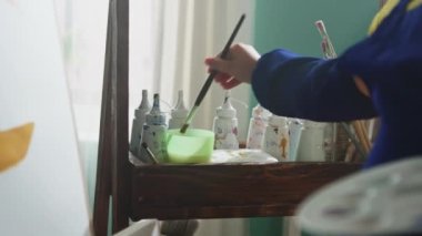 Çocuk fırçayı temizliyor ve boyaya koyuyor