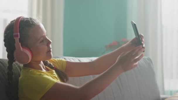 Mädchen in rosa Headsets macht Selfie auf Sofa — Stockvideo