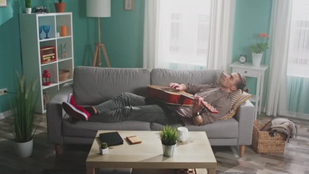 Молодой человек расслабляется, играя на гитаре — стоковое видео