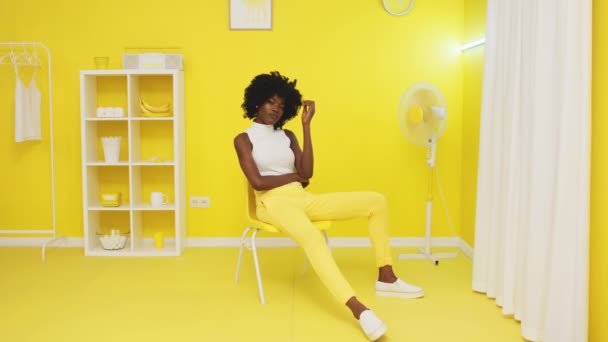 Αφρικανική γυναίκα κάθεται στο κίτρινο γραφείο και κοιτάζοντας κάμερα — Αρχείο Βίντεο