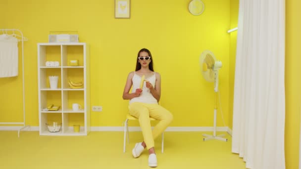 年轻女子在黄色办公室剥皮香蕉 — 图库视频影像