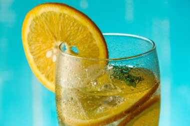 Geleneksel buzlu yaz kokteyli, köpüklü su, dilimlenmiş portakal ve nane, mavi arka planda dönüyor..