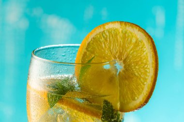 Geleneksel buzlu yaz kokteyli, köpüklü su, dilimlenmiş portakal ve nane, mavi arka planda dönüyor..