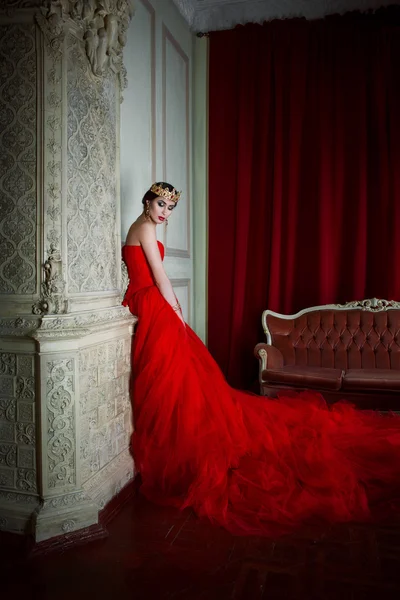 Güzel kız uzun kırmızı elbise ve şömine yakınındaki royal crown