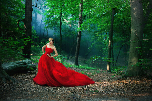 Woman in a long red dress and a royal crown in the foggy forest