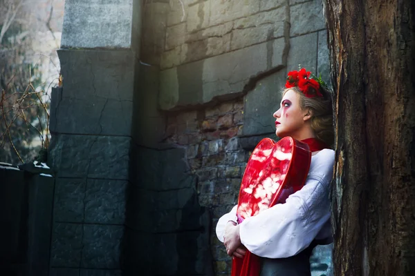 Giovane ragazza bionda in camicia nazionale ucraina e con corona di papaveri e grande cuore rosso nelle sue mani piangendo lacrime di sangue nel cimitero — Foto Stock