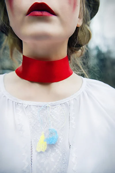 Menina loira jovem em blusa ucraniana nacional e com coroa de papoilas e grande coração vermelho em suas mãos chorando lágrimas sangrentas no cemitério — Fotografia de Stock