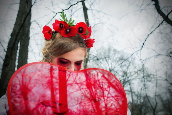 Jong blond meisje in nationale Oekraïense blouse en met krans van klaprozen en groot rood hart in haar handen huilen bloederige tranen op het kerkhof — Stockfoto