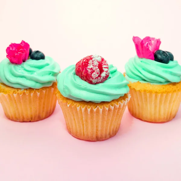 Cupcakes à la crème au beurre et vanille à la framboise et myrtille avec des fleurs roses sur fond rose — Photo