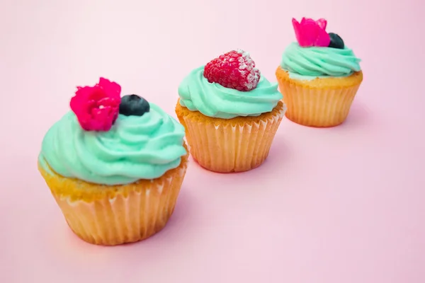 Cupcakes con crema de mantequilla y vainilla con frambuesa y arándanos con flores rosadas sobre fondo rosa —  Fotos de Stock