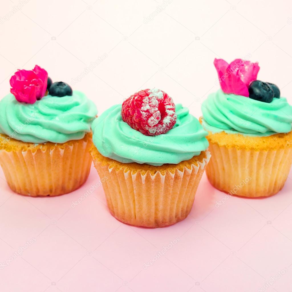 Cupcakes with butter cream and vanilla with blueberry and raspberry with pink flowers on pink background