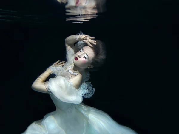 Jong meisje in lange witte luxe jurk onderwater op de zwarte achtergrond — Stockfoto