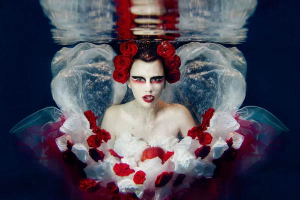 Mädchen im Kleid aus weißen und roten Rosen unter Wasser — Stockfoto