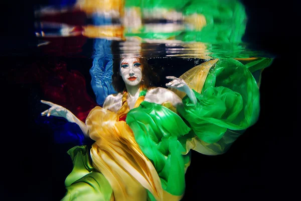 Kızıl saçlı kız büyük deniz kabuğu su altında koyu arka plan üzerinde renkli giysiler ile