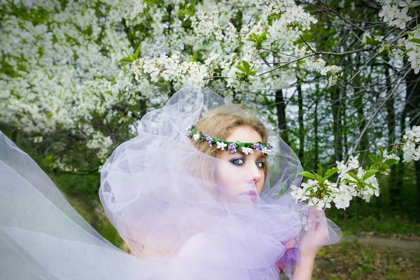 Hermosa chica rubia joven en los árboles en flor en primavera —  Fotos de Stock