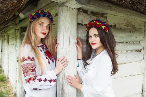 Dos chicas hermosas jóvenes con el pelo largo en blusas ucranianas y en una corona de flores en la aldea étnica al aire libre Pirogovo en Kiev Ucrania —  Fotos de Stock