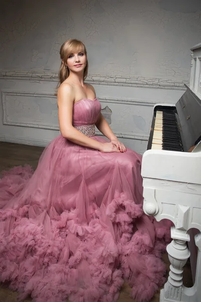 Retrato de menina bonita jovem em vestido rosa longo perto do piano — Fotografia de Stock