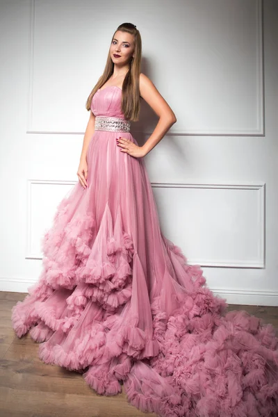 Portrait of young beautiful girl in long pink dress in white room — Stock Photo, Image