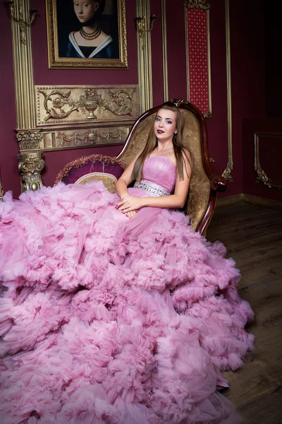 Ritratto di giovane bella ragazza in abito rosa lungo seduta sul divano retrò — Foto Stock
