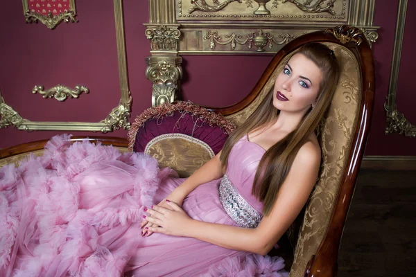 Retrato de menina bonita jovem em vestido rosa longo sentado no sofá retro — Fotografia de Stock