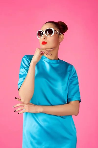 Retrato de mujer hermosa joven en vestido de seda azul y gafas de sol blancas ot el fondo rosa — Foto de Stock