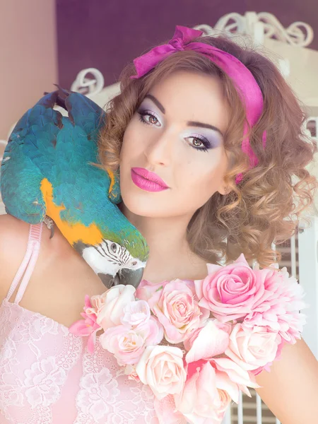 Retrato de jovem mulher bonita em vestido colorido com flores em estilo boneca com ara em seu ombro — Fotografia de Stock