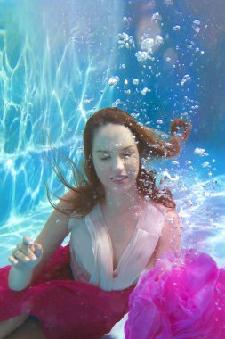 Genç gülümseyen güzel yüzme havuzunda sualtı elbiseli kadın beyaz