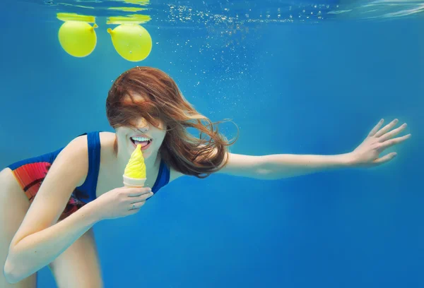 Piękna dziewczyna czerwone włosy uśmiechający się jeść żółty lody w basenie pod wodą w lecie — Zdjęcie stockowe