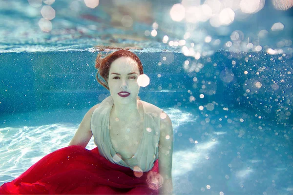 Lächelnde junge schöne weiße Frau im Kleid unter Wasser im Schwimmbad — Stockfoto