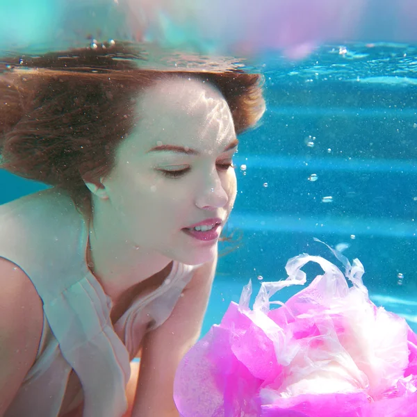 Jonge mooie witte vrouw in jurk met roze bloem onder water in het zwembad — Stockfoto