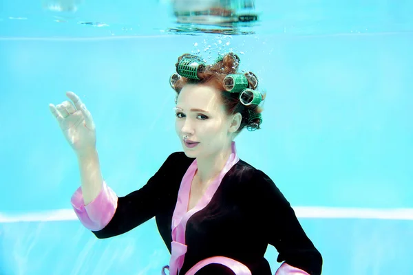 Young girl in a bathrobe and curlers  underwater in the swimming pool — Stock Photo, Image