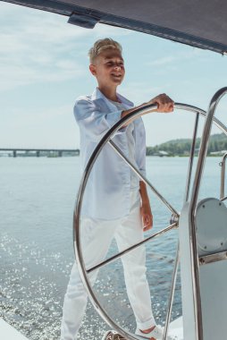 Beyaz tişörtlü ve yelkenli yatlı, gülümseyen sarışın çocuk. Eğitim, dersler, öğrenim, beceriler, tatil, büyüme kavramı