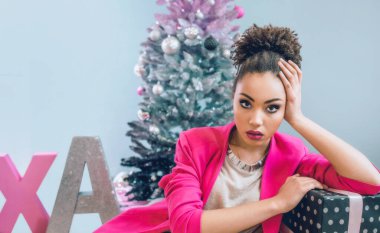 Noel ağacının yanındaki üzgün Afro-Amerikalı kadın Noel hediyesi yüzünden hayal kırıklığına uğradı. Noel, yeni yıl, hüsran, mutluluk, tatil konsepti