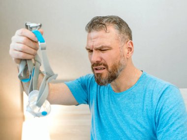 Mutsuz, şok olmuş, kronik solunum sorunu olan bir adam yatak odasında CPAP makinesini kullanarak şaşırdı. Sağlık, CPAP, uyku apnesi terapisi, horlama konsepti