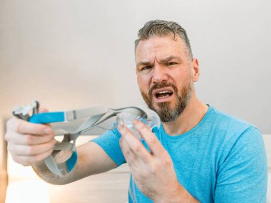 Mutsuz, şok olmuş, kronik solunum sorunu olan bir adam yatak odasında CPAP makinesini kullanarak şaşırdı. Sağlık, CPAP, uyku apnesi terapisi, horlama konsepti