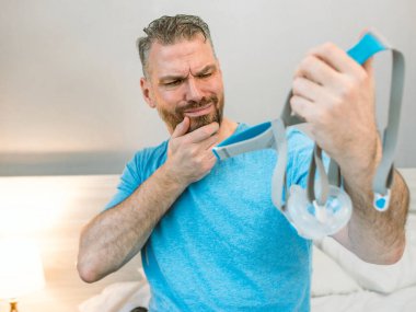 Mutsuz, şok olmuş, kronik solunum sorunu olan bir adam yatak odasında CPAP makinesini kullanarak şaşırdı. Sağlık, CPAP, uyku apnesi terapisi, horlama konsepti
