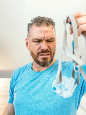Mutsuz, şok olmuş, kronik solunum sorunu olan bir adam yatak odasında CPAP makinesini kullanarak şaşırdı. Sağlık, CPAP, uyku apnesi terapisi, horlama konsepti
