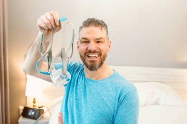 Kronik solunum sorunu olan olgun, mutlu bir adam yatak odasında CPAP makinesiyle yatmayı düşünüyor. Sağlık, CPAP, horlama konsepti