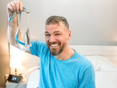 Kronik solunum sorunu olan olgun, mutlu bir adam yatak odasında CPAP makinesiyle yatmayı düşünüyor. Sağlık, CPAP, horlama konsepti