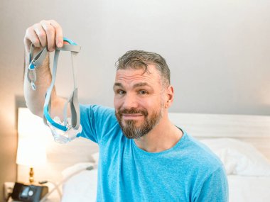 Kronik solunum sorunu olan olgun, mutlu bir adam yatak odasında CPAP makinesiyle yatmayı düşünüyor. Sağlık, CPAP, horlama konsepti